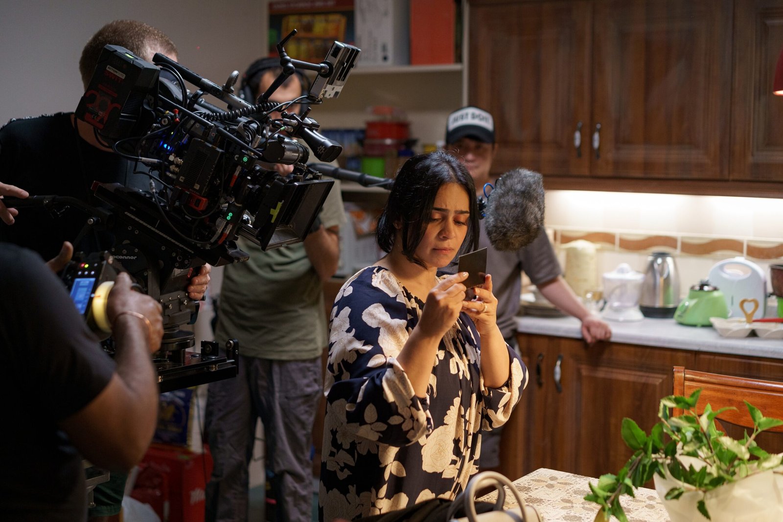 A performer holding a cup on HOBA’s kitchen set, surrounded by camera and sound crew