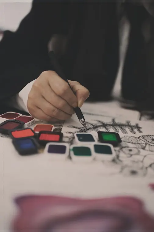 Huihui painting a botanical design beside small pans of coloured pigment