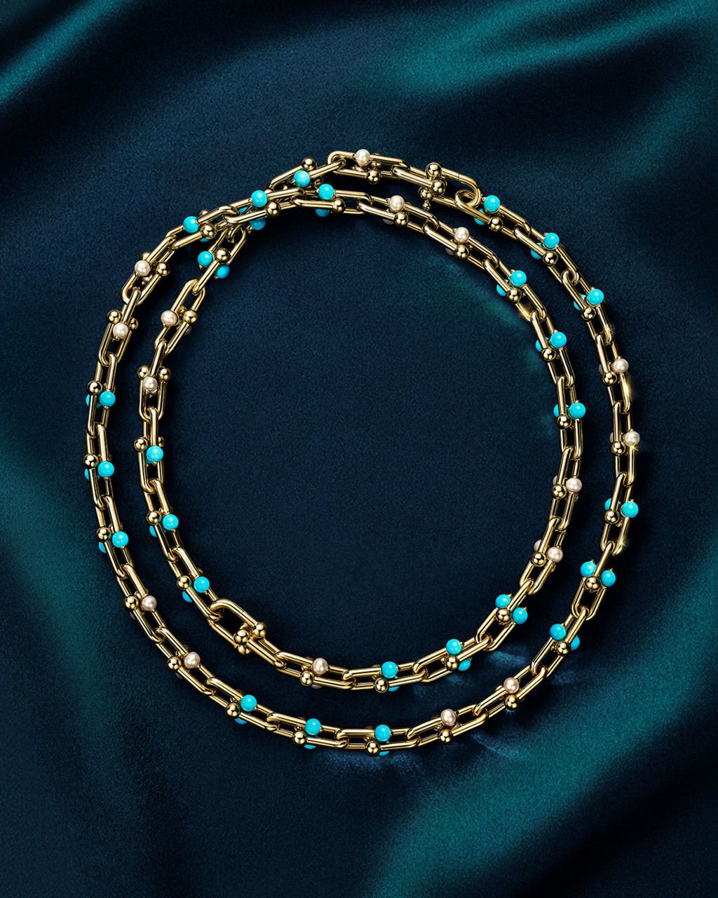Tiffany HardWear transformable gold necklace with turquoise beads and Akoya pearls arranged in two loops on dark teal fabric