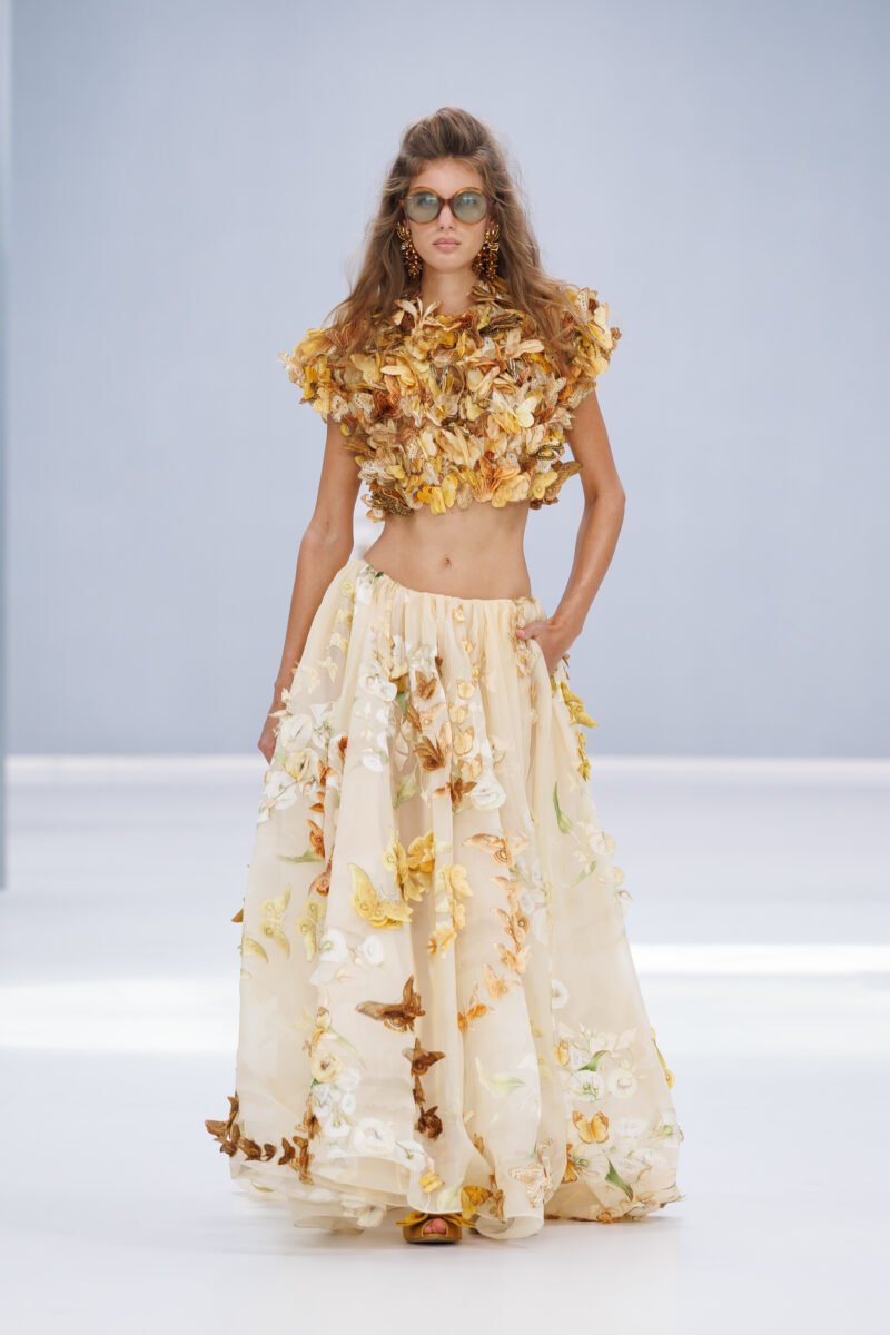 Zimmermann’s Spring 2027 opening look pairs a gilded butterfly-and-petal bodice with a botanical skirt