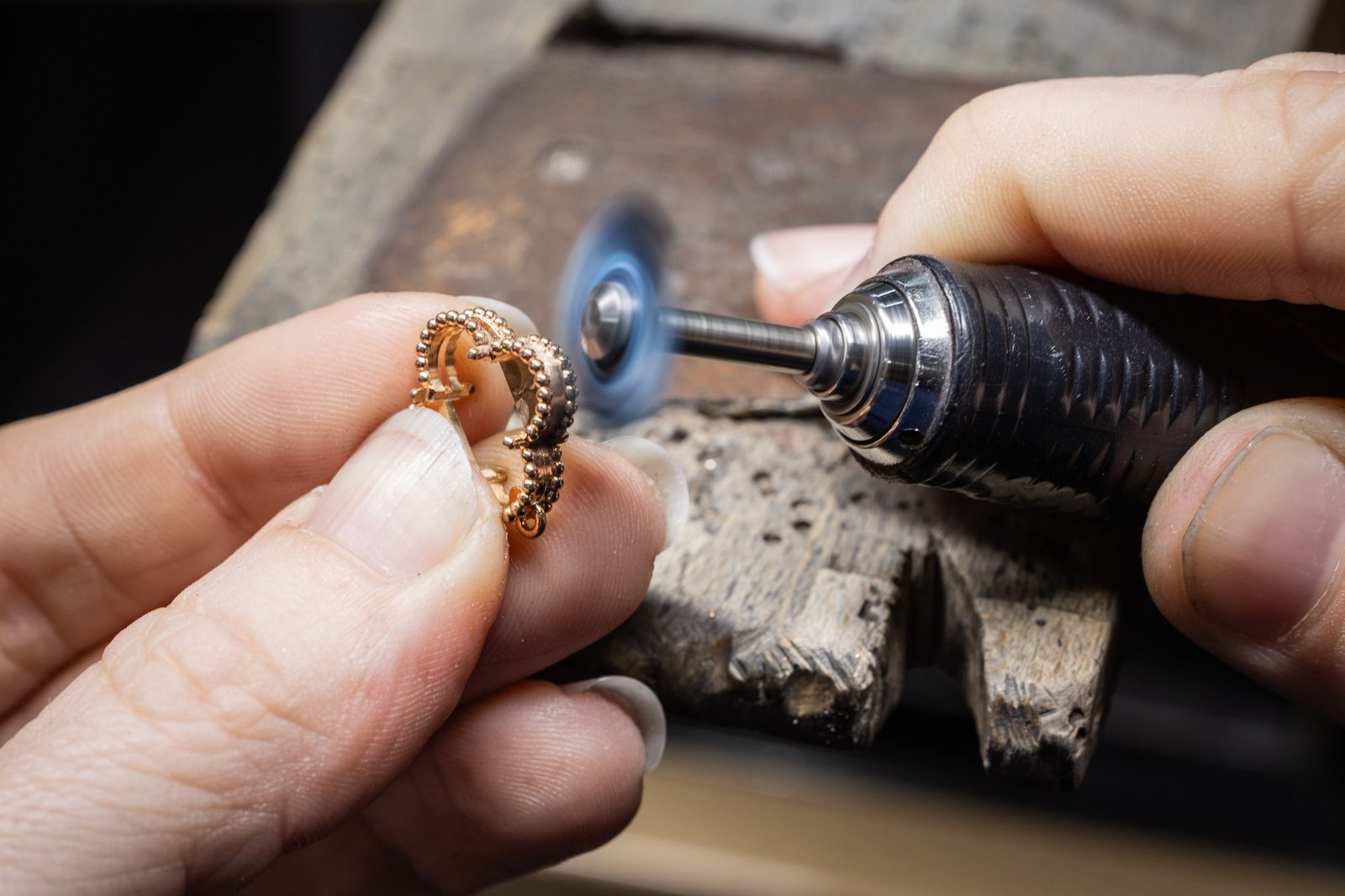 An artisan uses a rotary tool on the beaded rose-gold structure of an Alhambra motif.