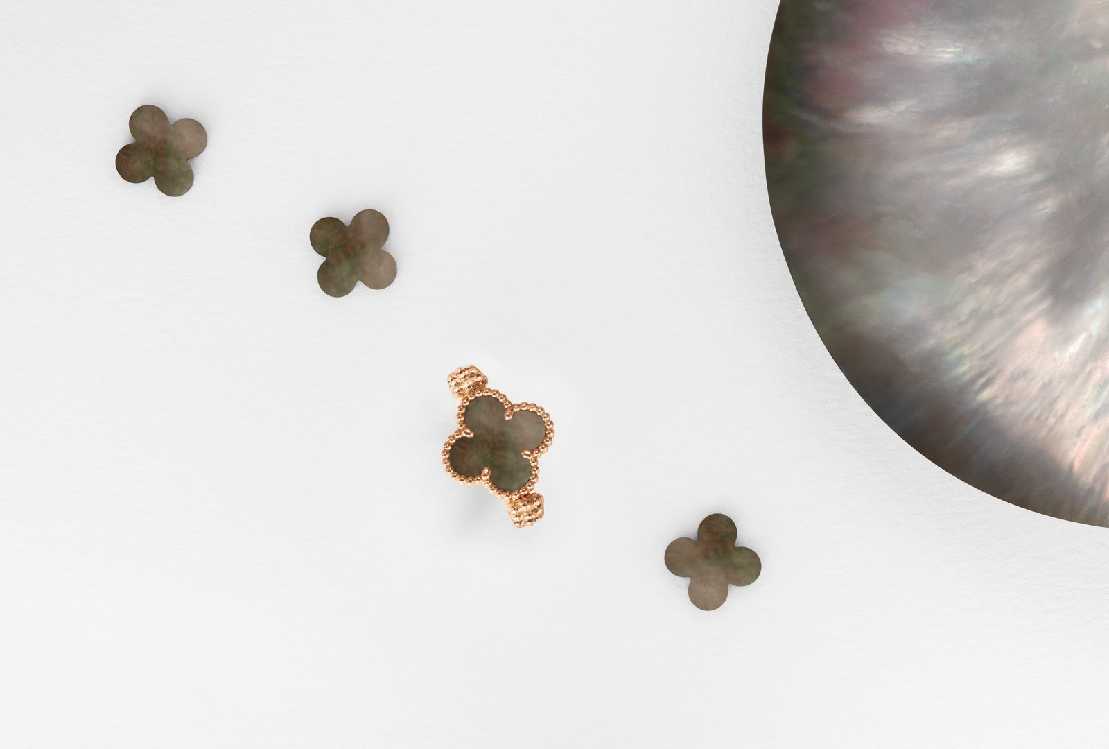 Rose-gold Vintage Alhambra reversible ring with its grey mother-of-pearl face visible beside loose motifs and a shell.