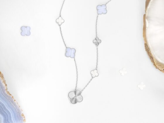 White-gold Magic Alhambra necklace with chalcedony and mother-of-pearl motifs, photographed with ornamental materials.