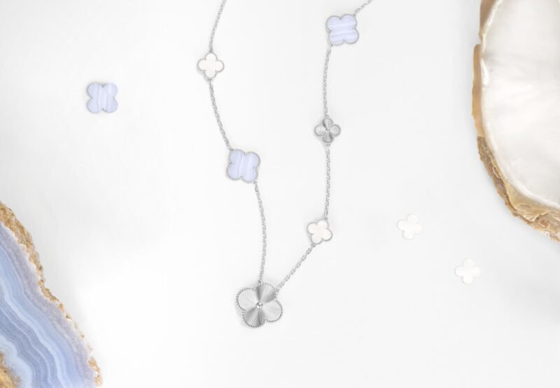 White-gold Magic Alhambra necklace with chalcedony and mother-of-pearl motifs, photographed with ornamental materials.