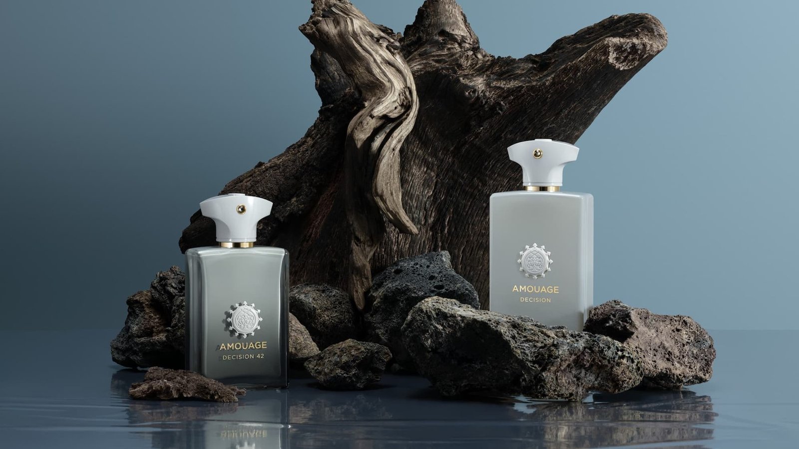Two Amouage Decision bottles arranged with dark sculptural wood against a grey background