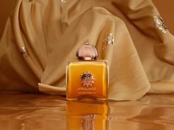 Amouage Overture41 bottle on a reflective amber surface in front of draped golden fabric