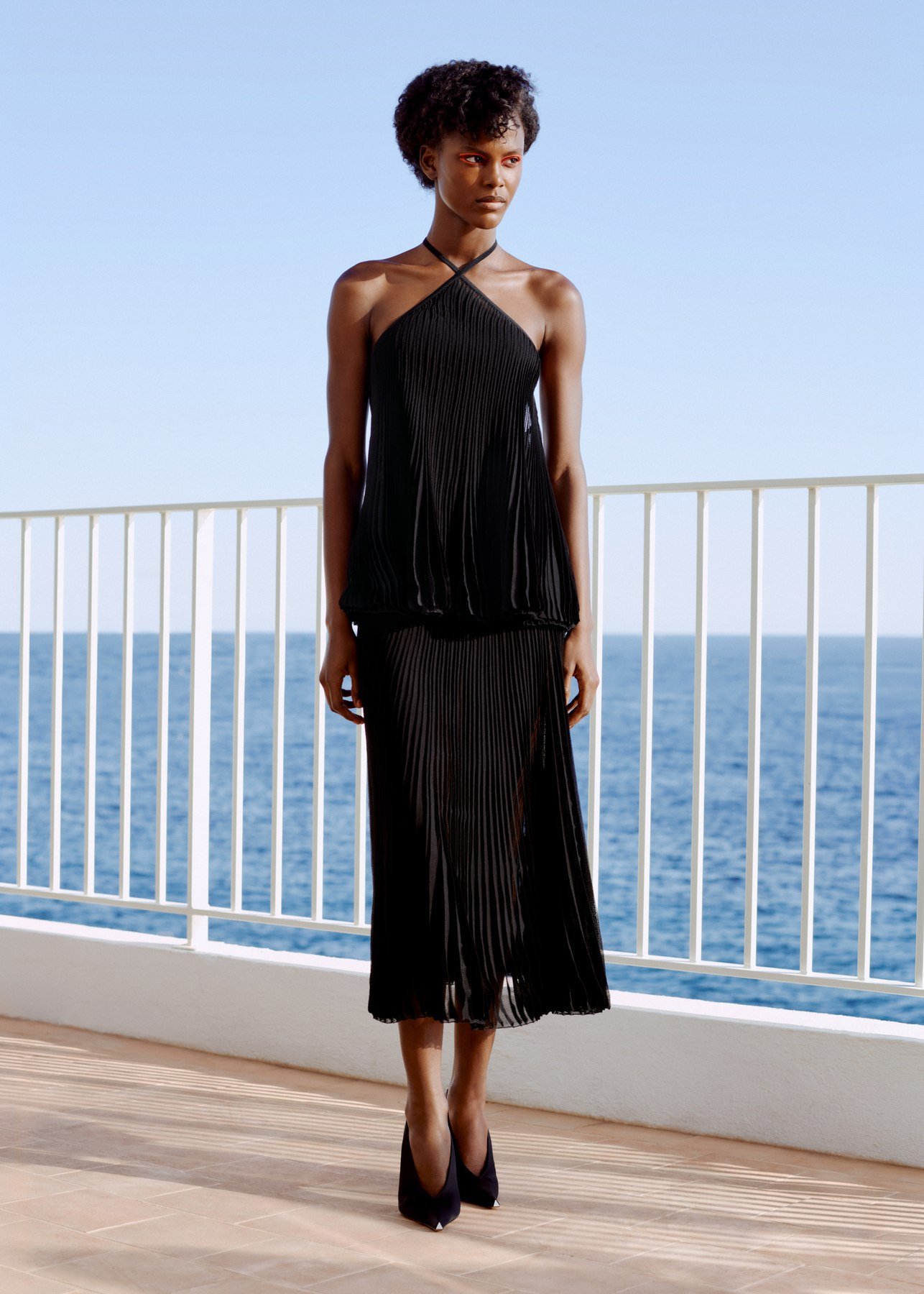 Black pleated ArdAzAei halter top and skirt photographed beside the sea