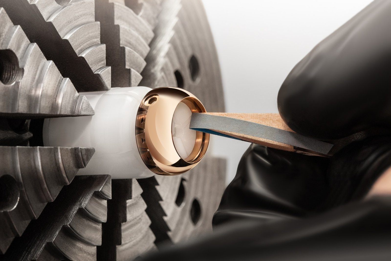 A polished Lady B case held in a machine chuck while a gloved craftsperson applies a finishing tool