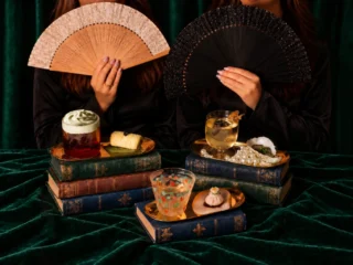 Three cocktail and canapé pairings arranged on books against green velvet, with beaded fans