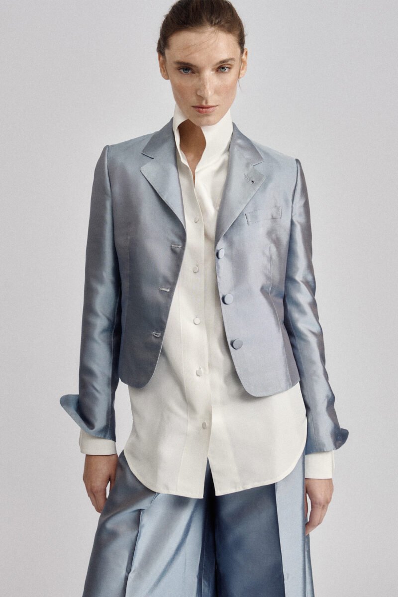 Model wearing a pale blue tailored jacket and matching trousers with an untucked white shirt.