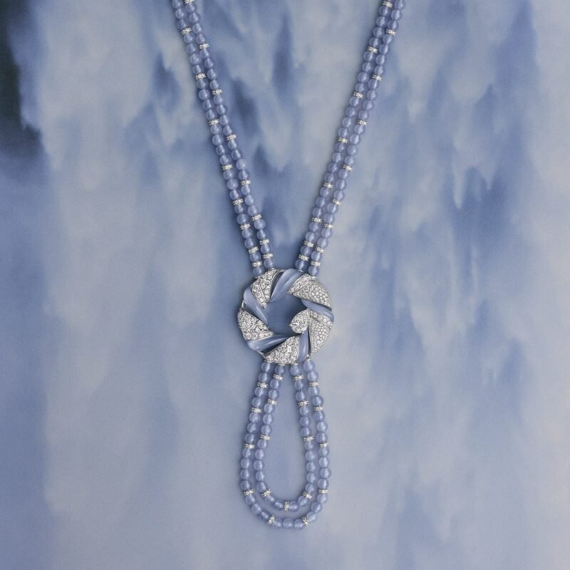 De Beers Cascade necklace with a diamond knot and looped strands against a blue textured background