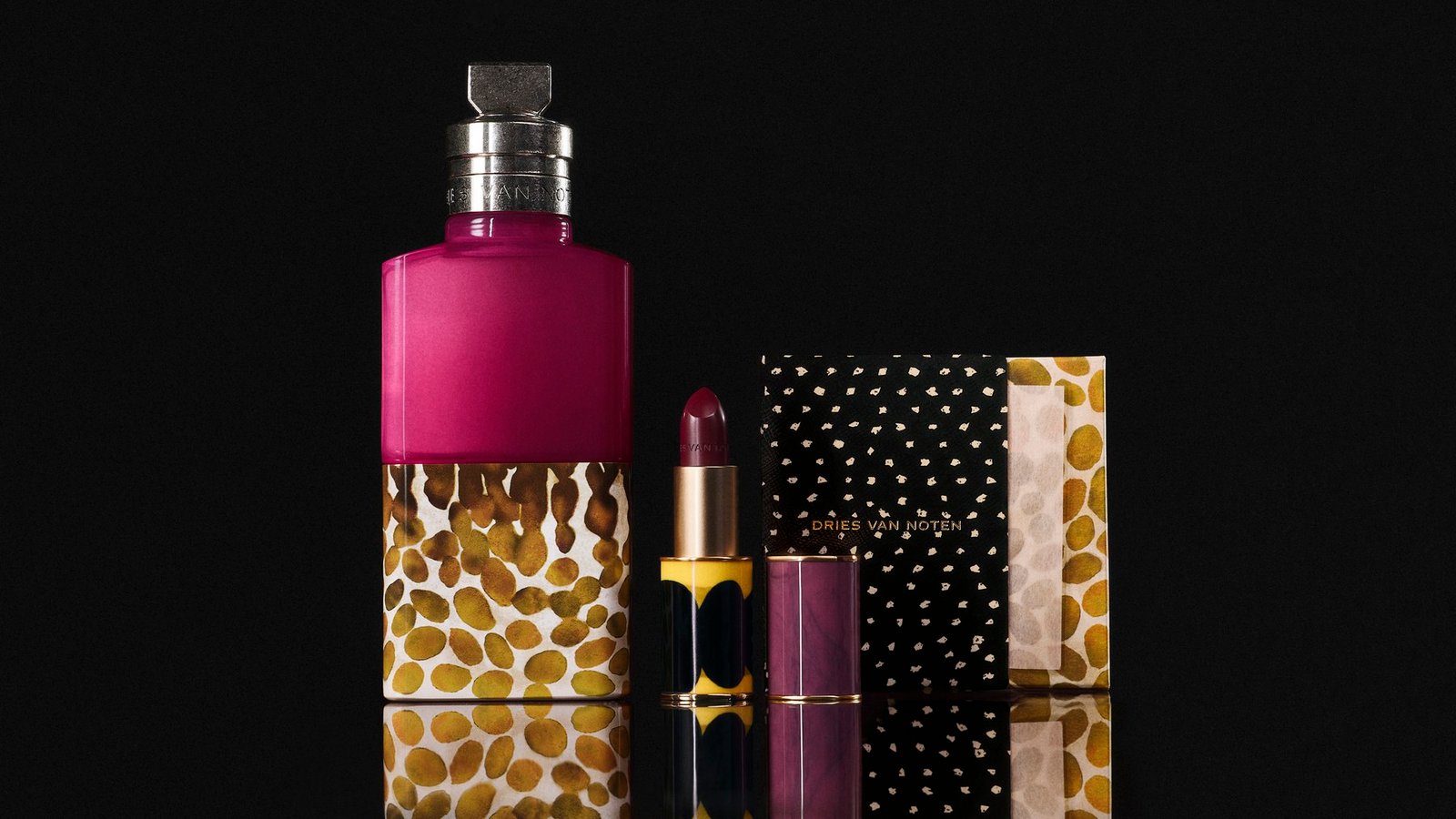 Velvet Violet perfume, an open lipstick and patterned beauty accessories arranged on a reflective black surface