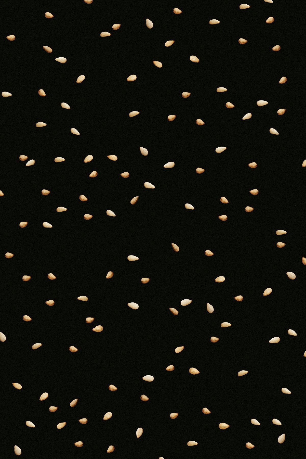 Pale sesame seeds scattered across a deep black background