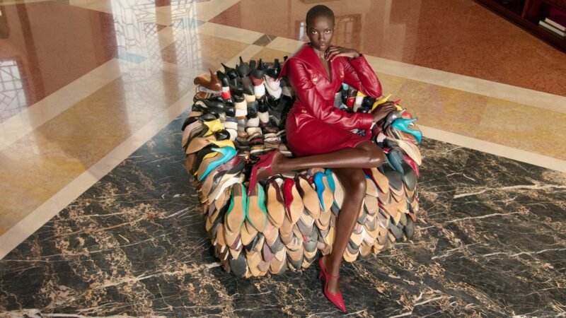 Anok Yai in a red dress seated on Willie Cole’s chair sculpture assembled from colourful shoes