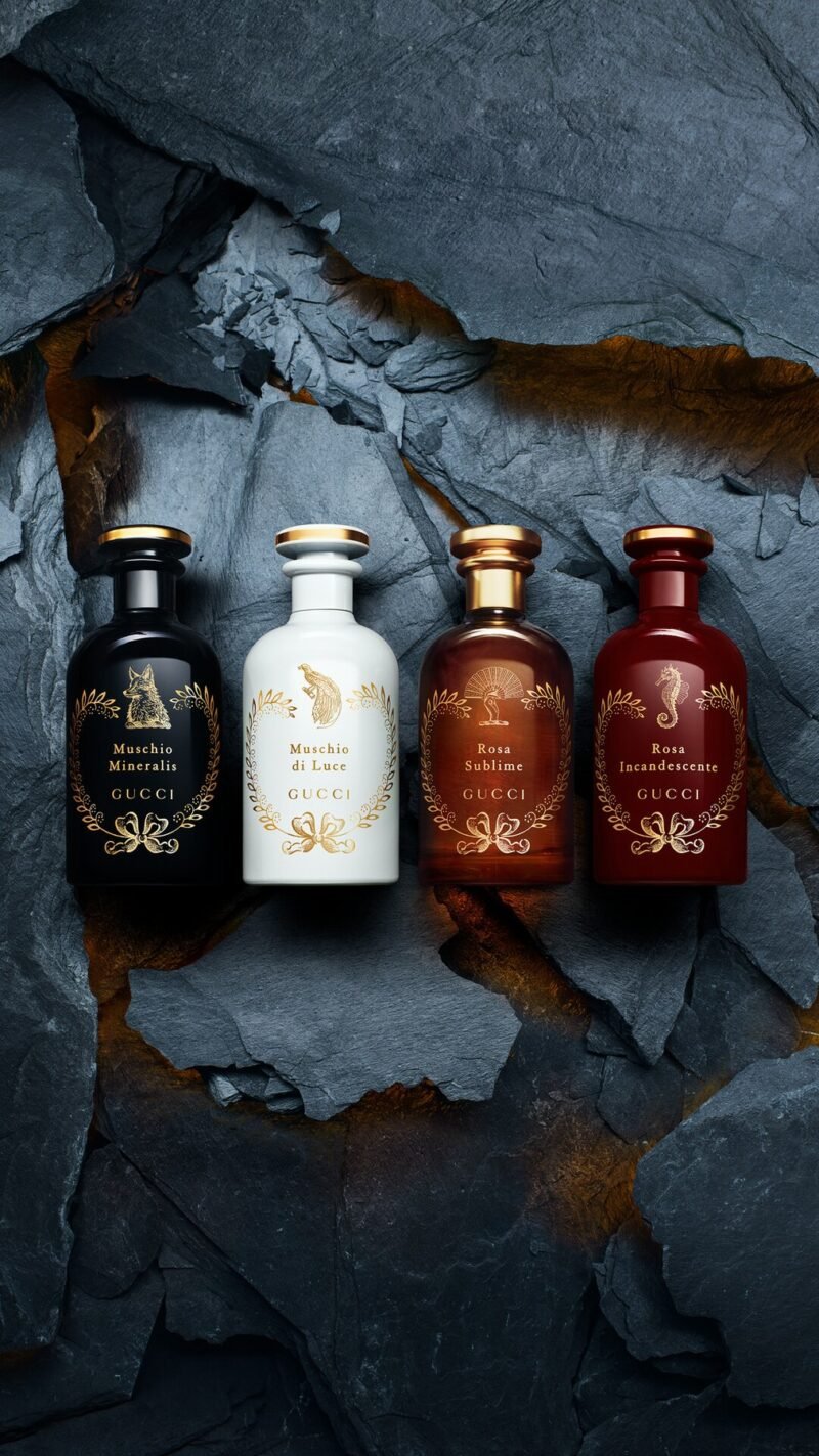 Four black, white, amber and red Gucci fragrance bottles arranged in a fissure in dark stone