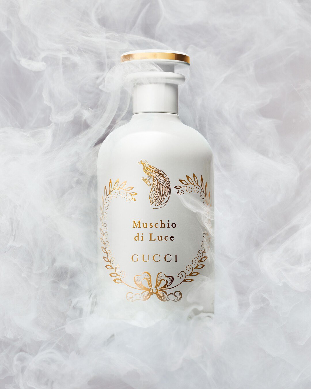 A white Muschio di Luce bottle with a golden bird motif surrounded by pale cloudlike forms