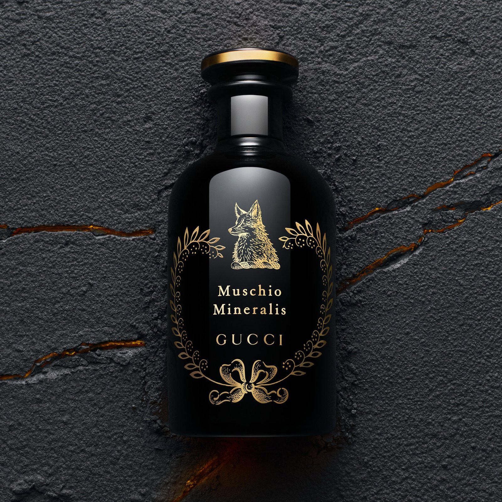 A black Muschio Mineralis bottle with a gold-coloured fox motif against fractured dark rock