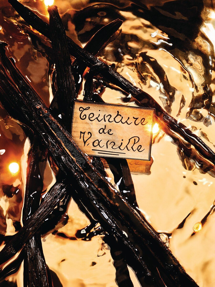 Dark vanilla pods and a handwritten Teinture de Vanille label surrounded by warm amber liquid