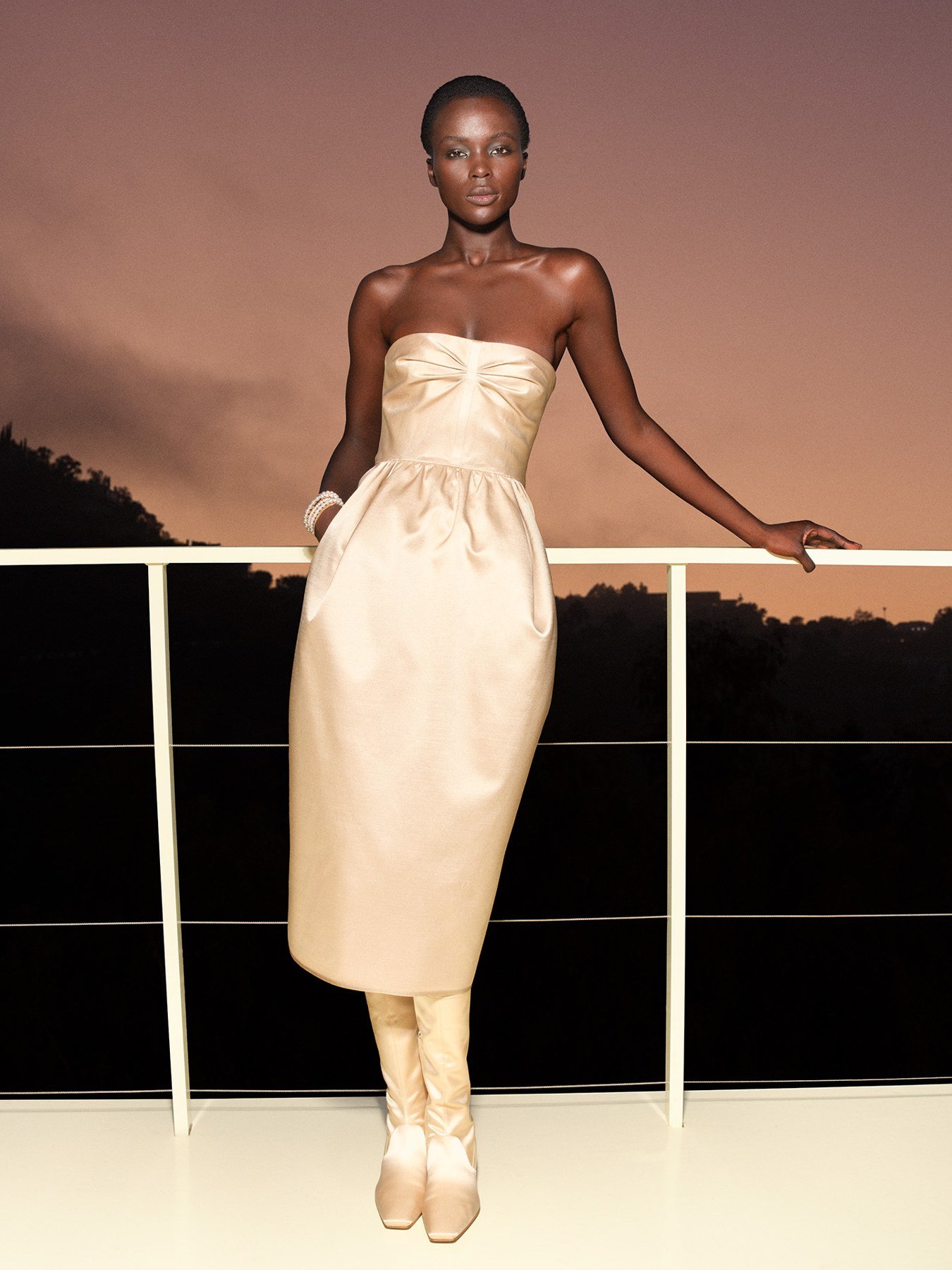 Model in a cream strapless Hermès dress and pale boots against a sunset sky