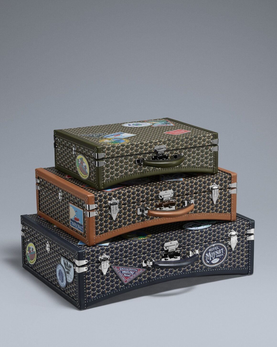 Three Hotel Moynat Limousine trunks in green, brown and navy with travel patches and metal hardware