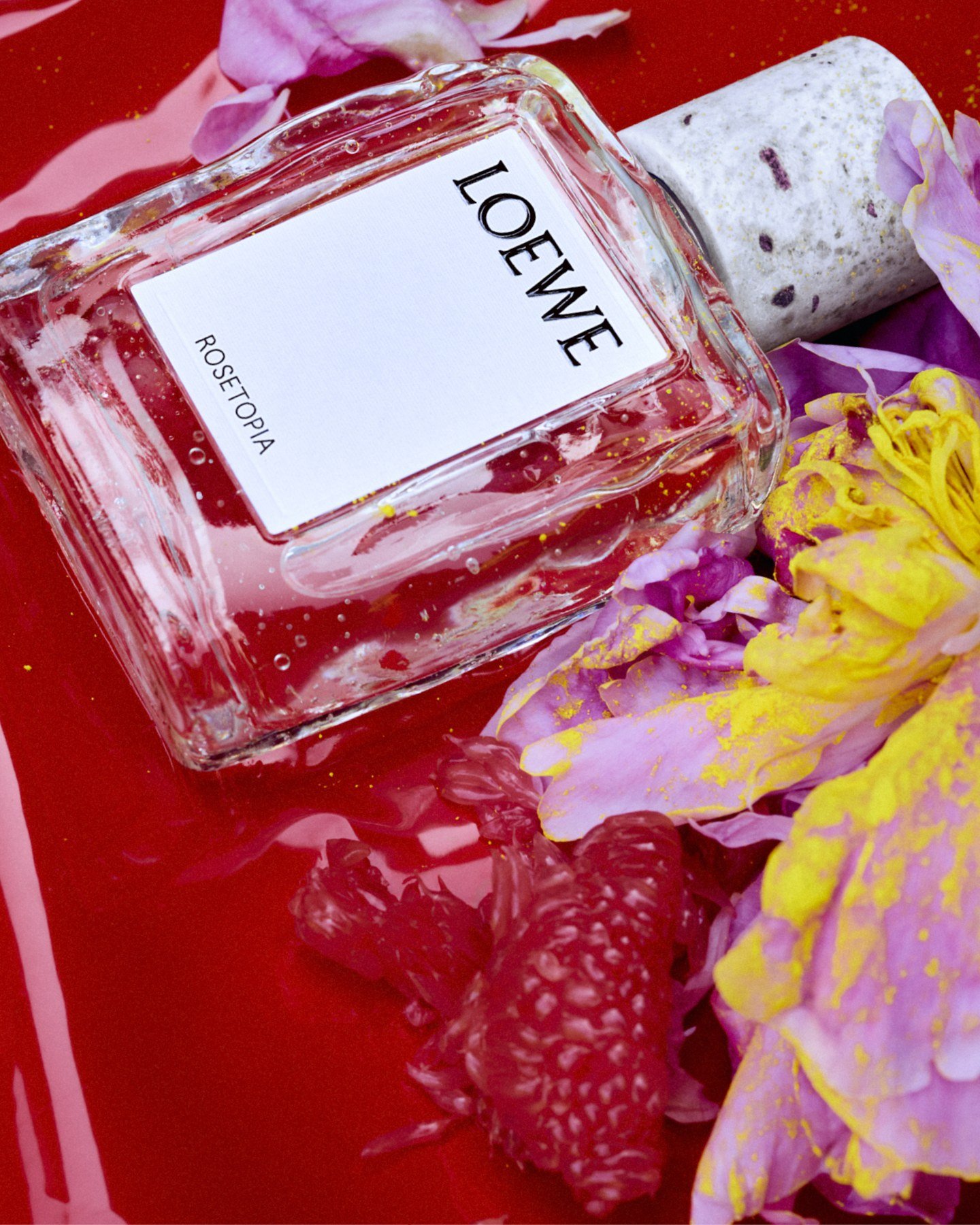 Loewe Rosetopia bottle against a vivid red background with pink and yellow flowers