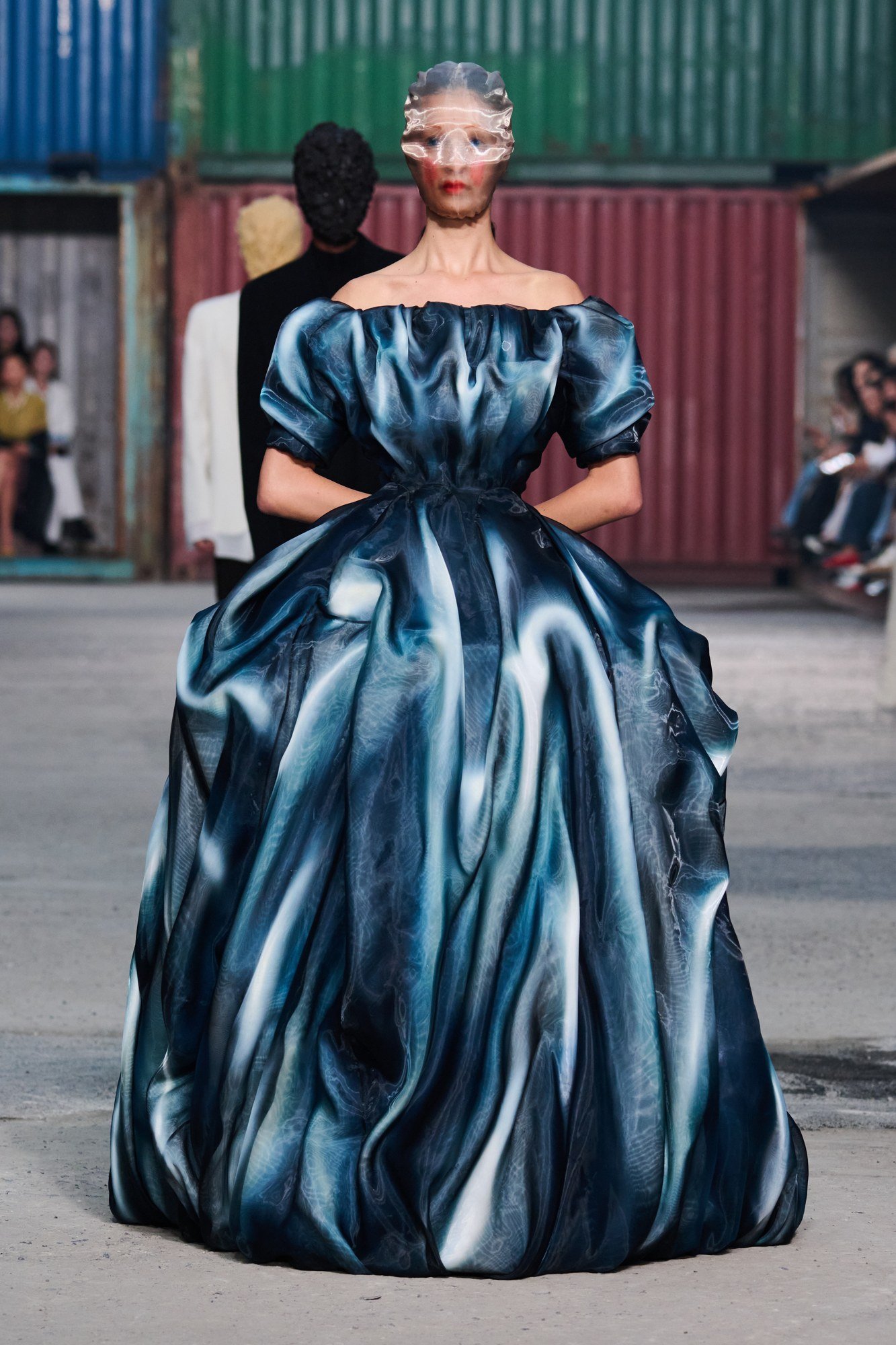 Front view of a voluminous blue gown with a cinched waist, short rounded sleeves and an Artisanal mask.
