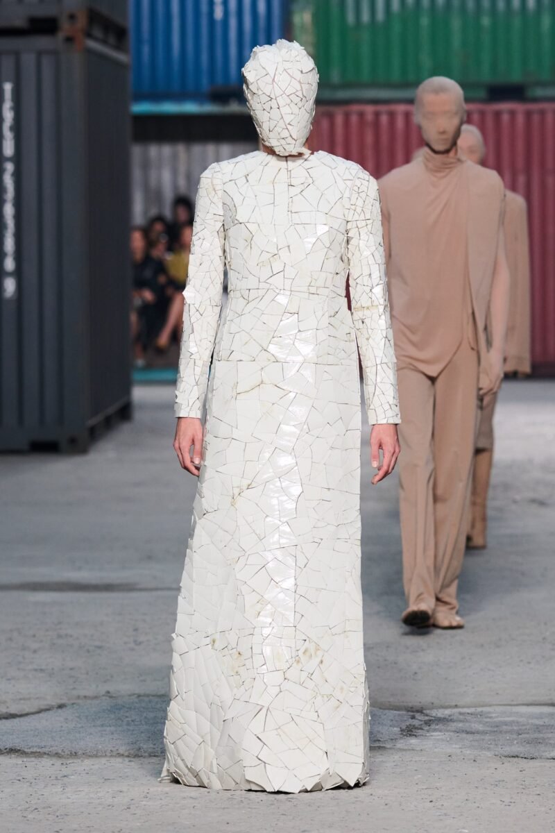 Front view of a long-sleeved white column dress and full-face mask formed from visible irregular fragments.