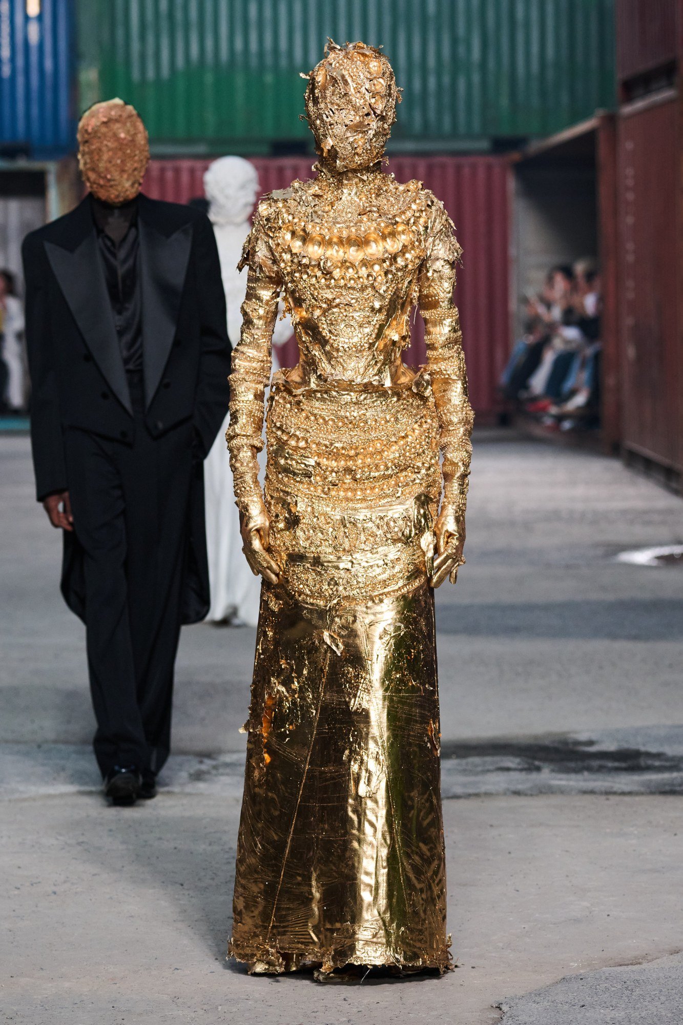 Front view of a long gold-tone dress, gloves and mask with an irregular sculpted surface and raised ornament across the torso.