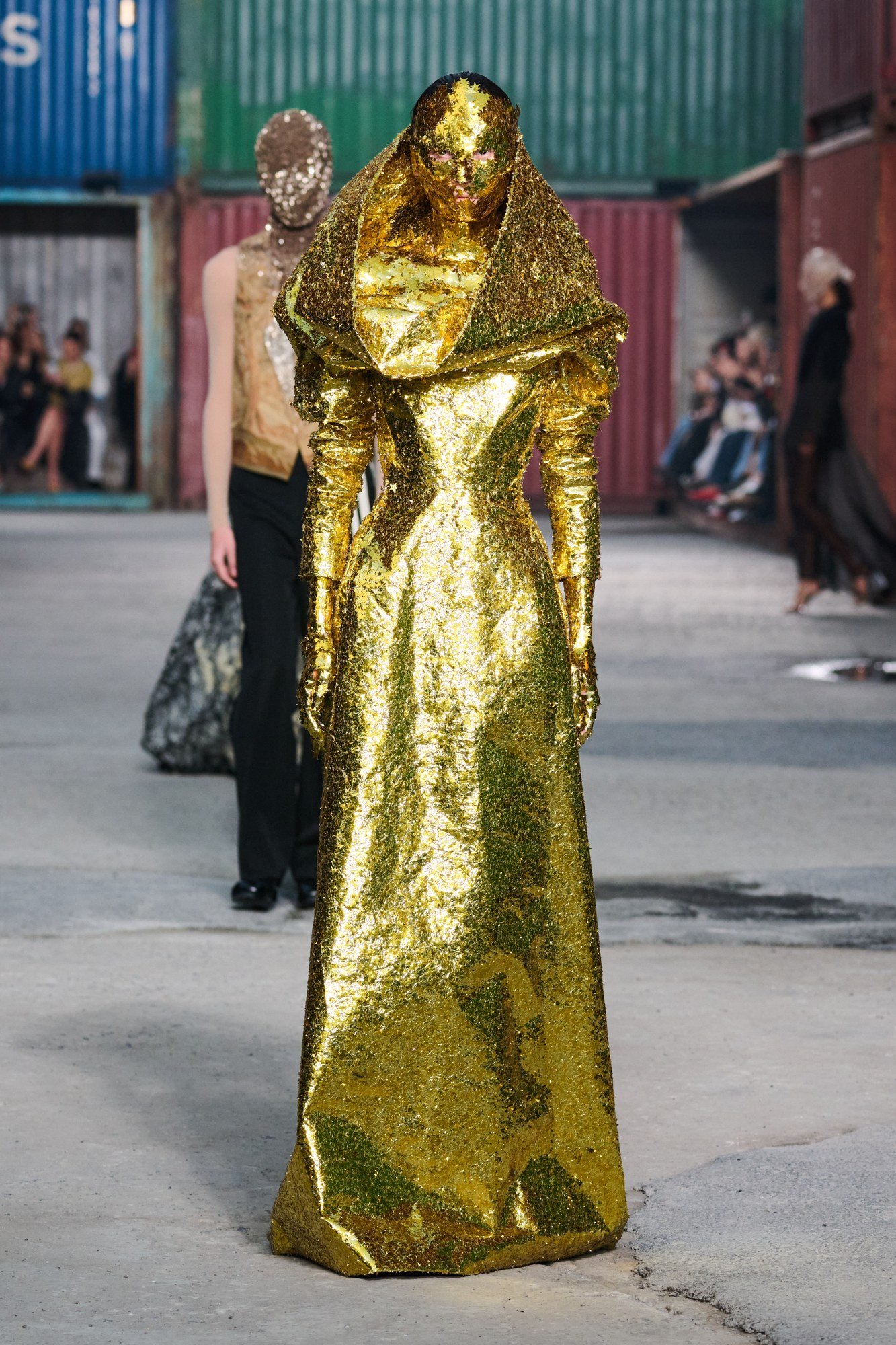 Front view of a gold-tone long dress with a large folded collar, defined waist, long sleeves and small star-shaped embellishments.