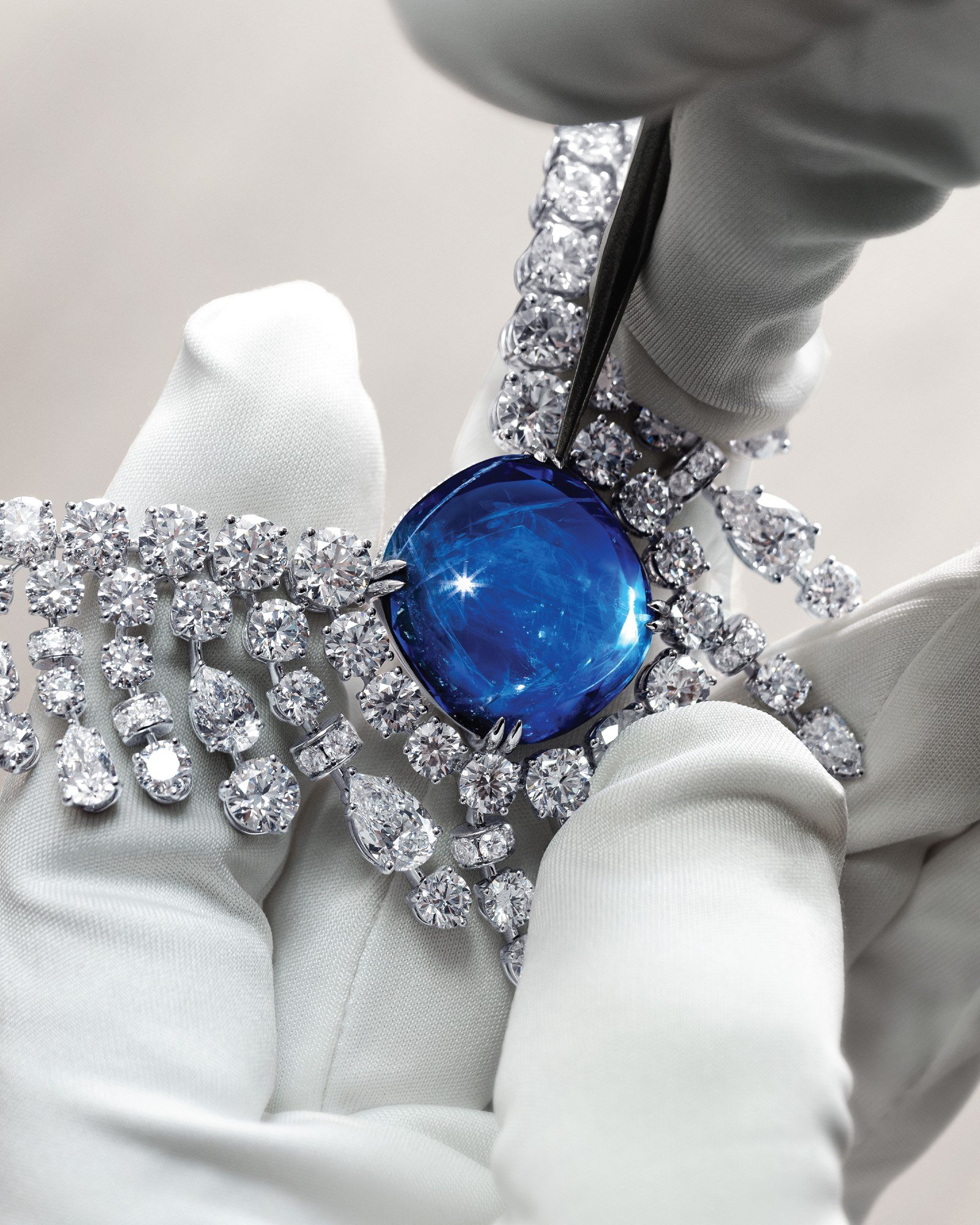 Gloved hands holding Mouawad’s Cascading Veil necklace near its central blue sapphire