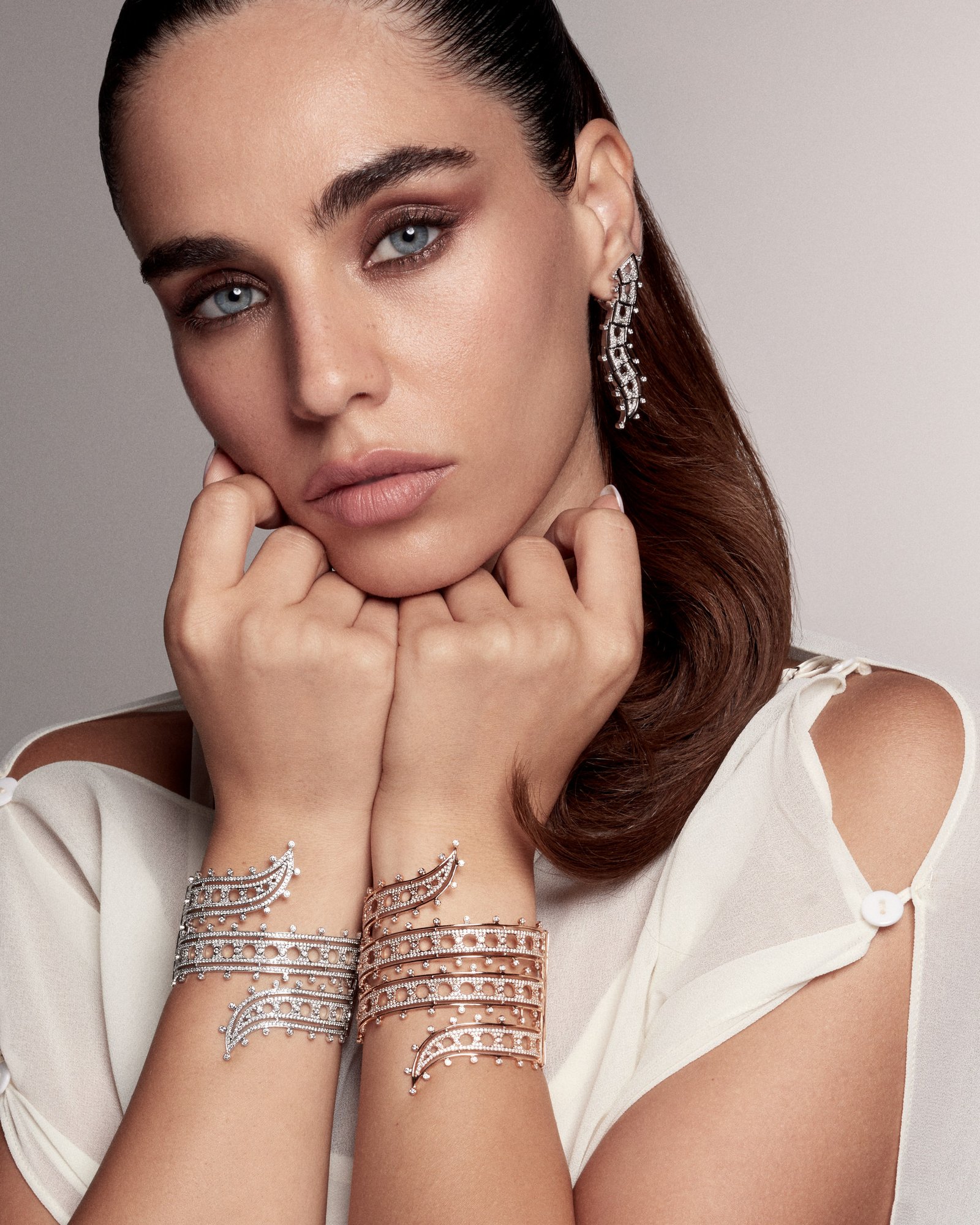 Model resting her chin on her hands, with wide openwork cuffs around both wrists and a long earring.