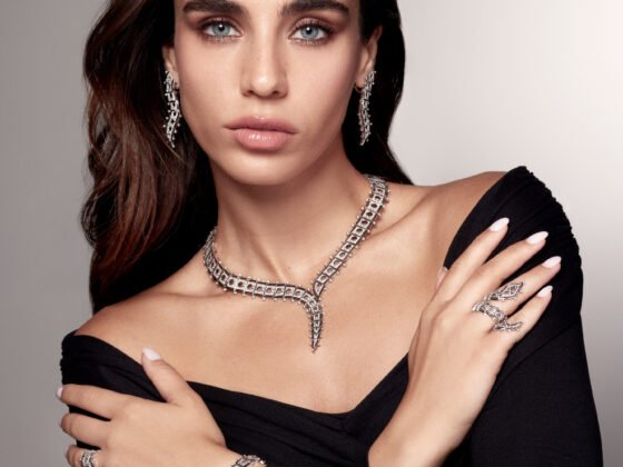 Model in a black off-the-shoulder top wearing a pointed necklace, drop earrings, rings and a linked hand ornament.