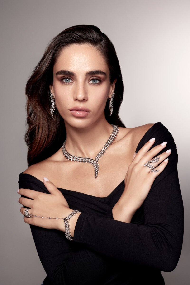 Model in a black off-the-shoulder top wearing a pointed necklace, drop earrings, rings and a linked hand ornament.