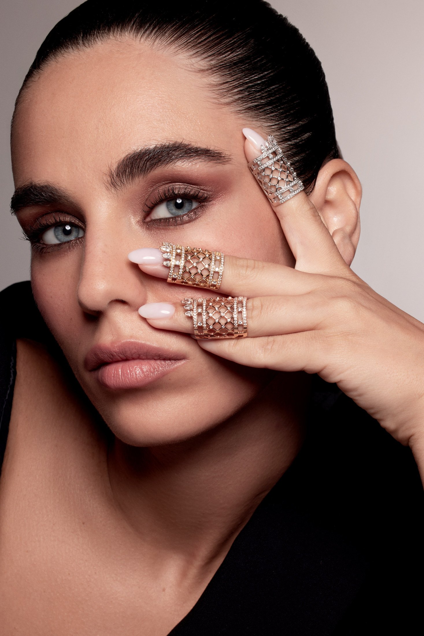 Close-up of three broad lattice-pattern rings on a model’s fingers held beside her face.