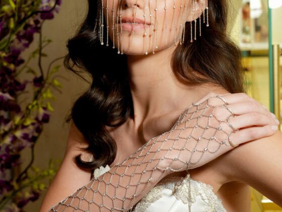 Model in a strapless ivory gown wearing fine chains across her face and an open lattice ornament over her forearm and hand.