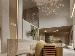 3D rendering of ORAA’s reception with a tall arch, sculptural cream seating, a pale counter and suspended gold-toned forms