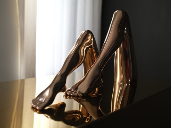 Two polished bronze sculptures of bent legs reflected in a dark tabletop