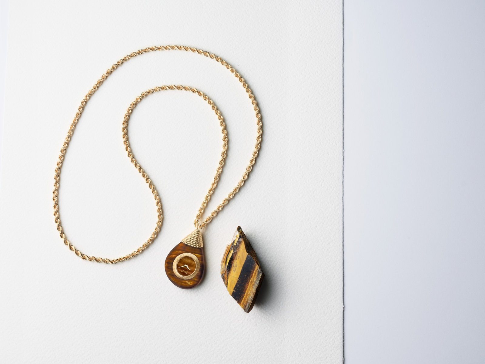 Swinging Pebbles G0A51410 in tiger’s eye and yellow gold, accompanied by a piece of the ornamental stone.