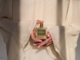 A model in ivory sleeves holds a square Shifa Kenza perfume bottle with ringed hands