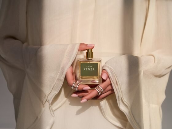 A model in ivory sleeves holds a square Shifa Kenza perfume bottle with ringed hands