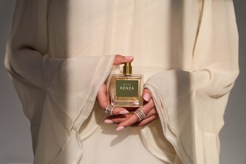A model in ivory sleeves holds a square Shifa Kenza perfume bottle with ringed hands