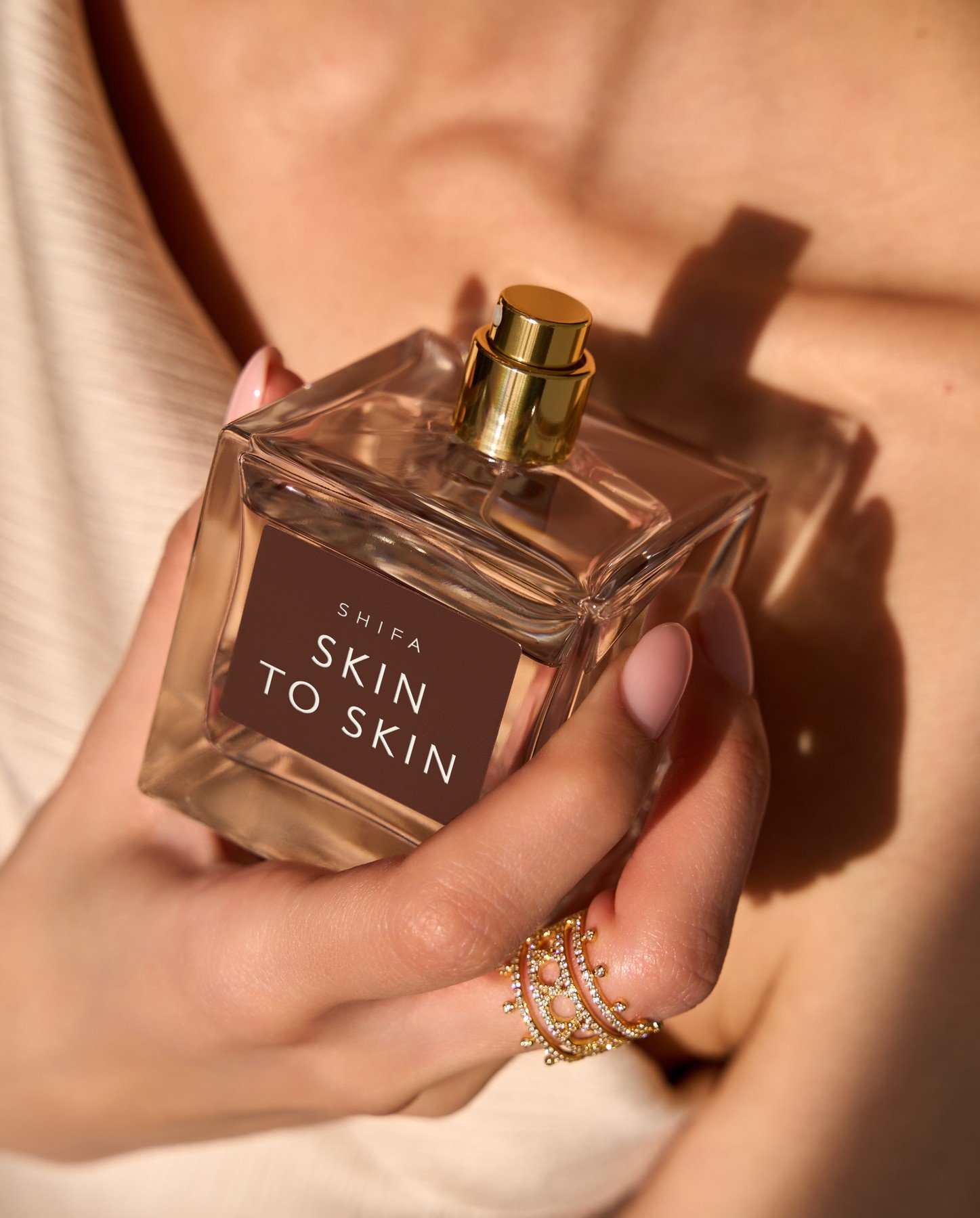 Close-up of a Shifa Skin To Skin perfume bottle held near a model’s collarbone