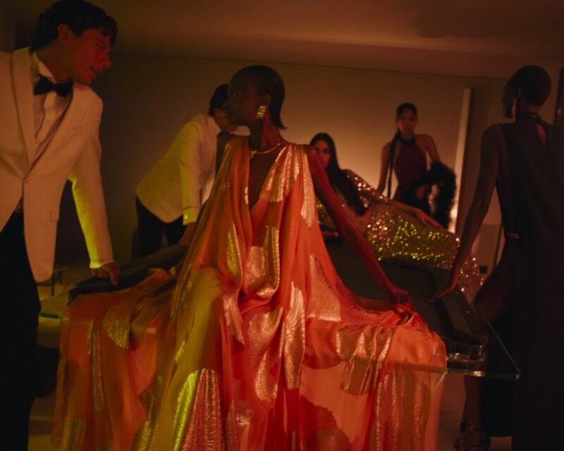Guests in luminous orange and gold eveningwear at an imagined villa party in Taller Marmo’s Mediterranea campaign