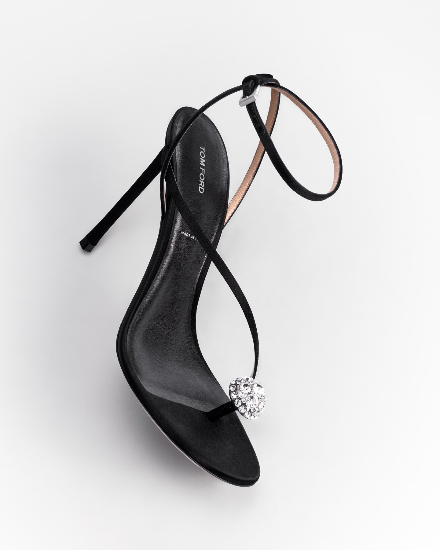 A black Tom Ford sandal with a fine ankle strap and a jewelled ornament at the thong