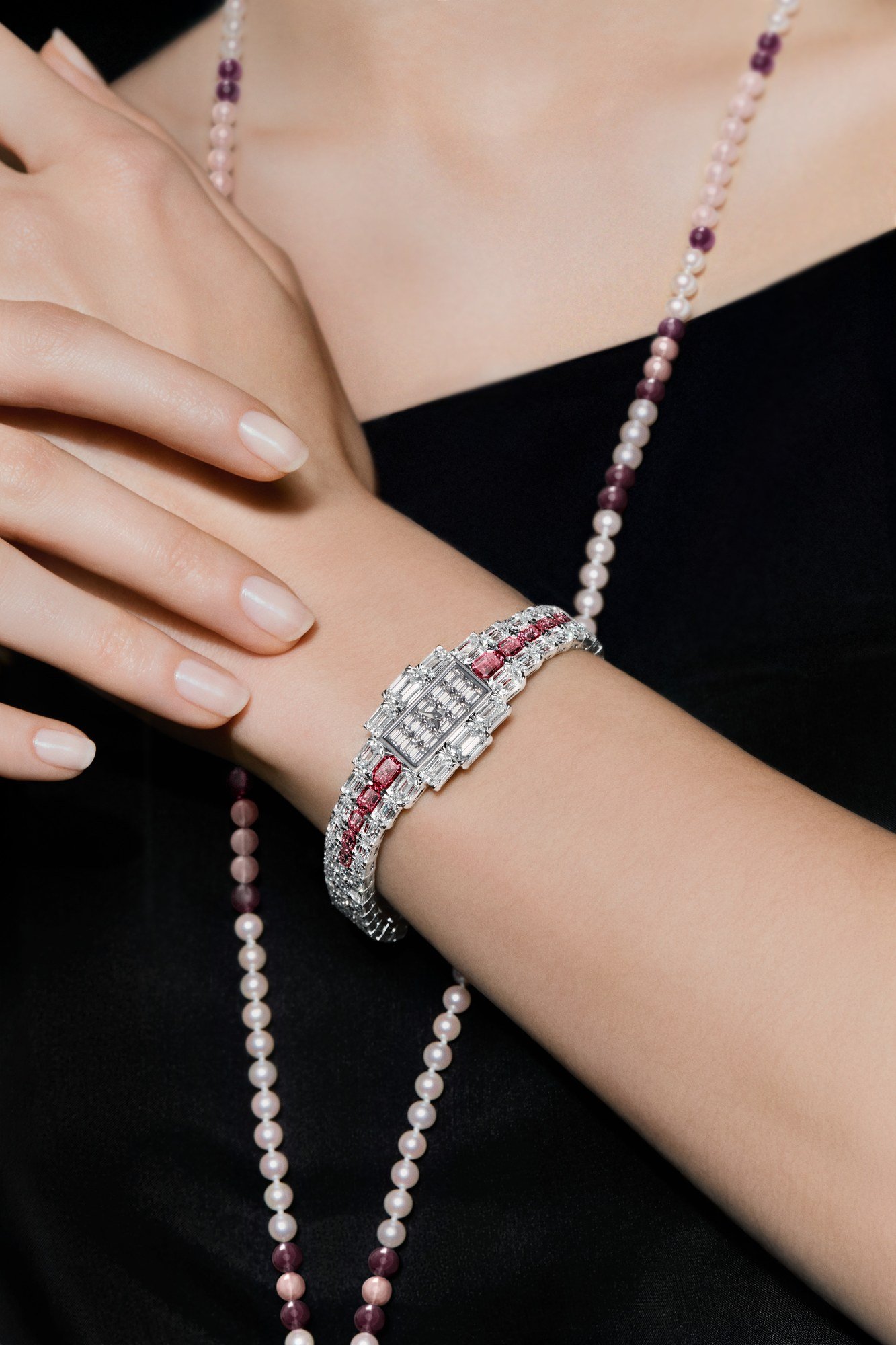 Ruby-set Grand Lady Kalla watch worn on the wrist beside a pearl and pink-stone necklace