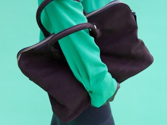 A soft dark bowling bag loops over the arm of a model wearing a vivid green top against a turquoise background